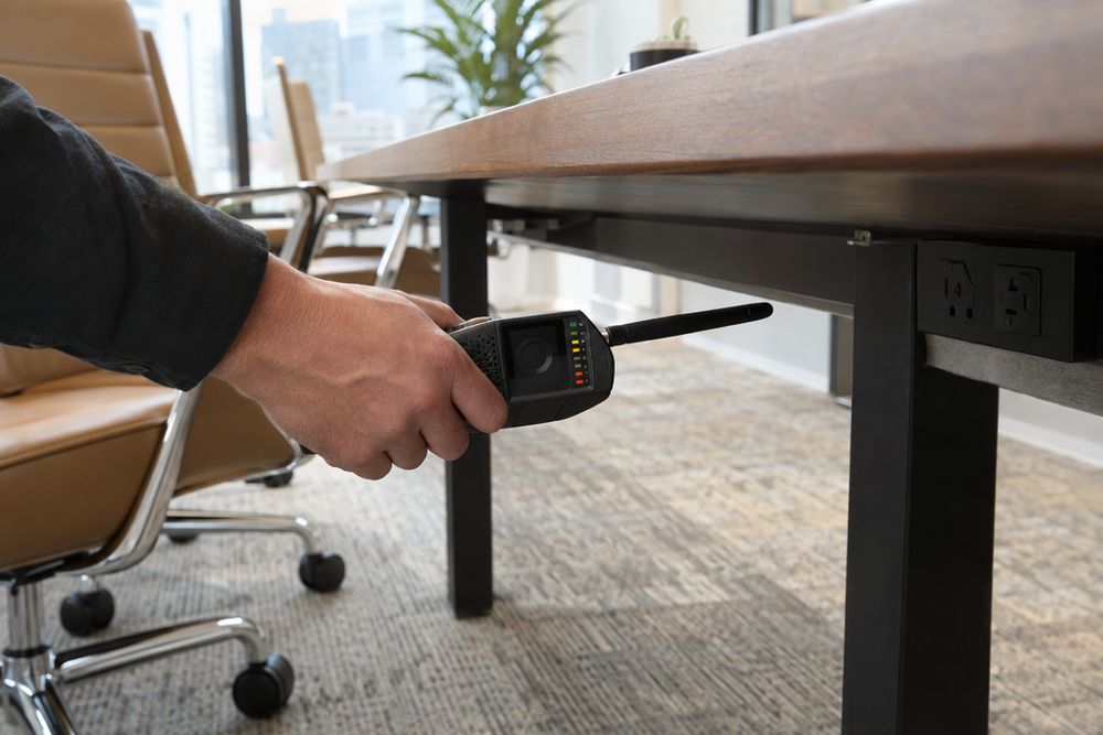 Mão segurando um detector de sinais sob a borda de uma mesa de reunião.